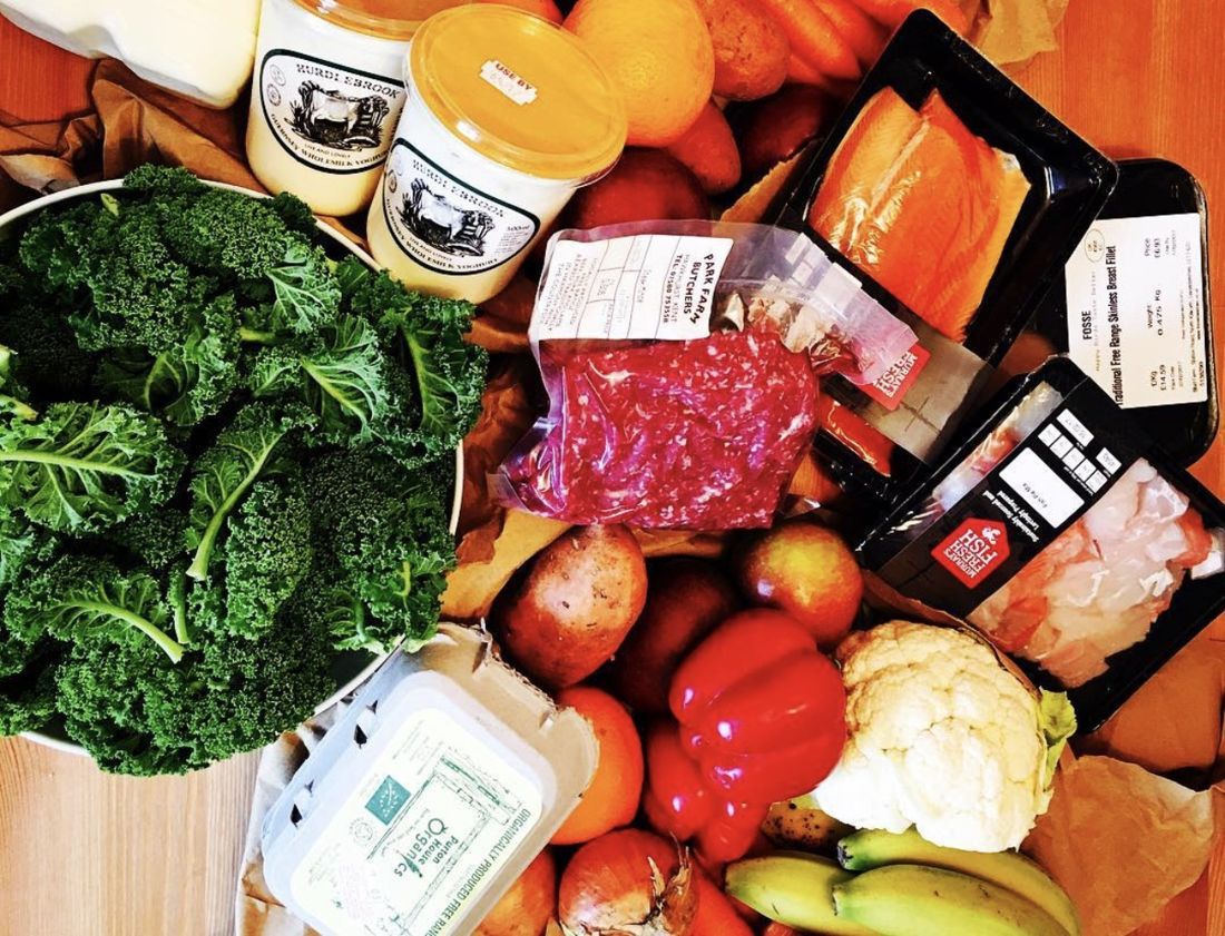 An organic delivery unpacked: a bowl of curly kale, whole milk and yoghurt from a farm dairy, free range eggs, salmon fillets, chicken, mince, cauliflower, peppers, carrots, bananas and a cabbage.