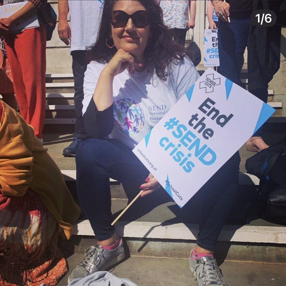 Yasmin sitting on stone steps at a protest, wearing a SEND National Crisis Hackney t shirt and holding a placard that reads End the SEND crisis. Other campaigners stand around her with their own placards.