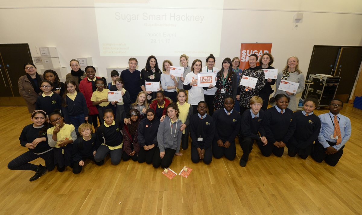 A large group photograph of all the schools and community groups in Hackney receiving their Sugar Smart certificates, standing together holding their certificates.